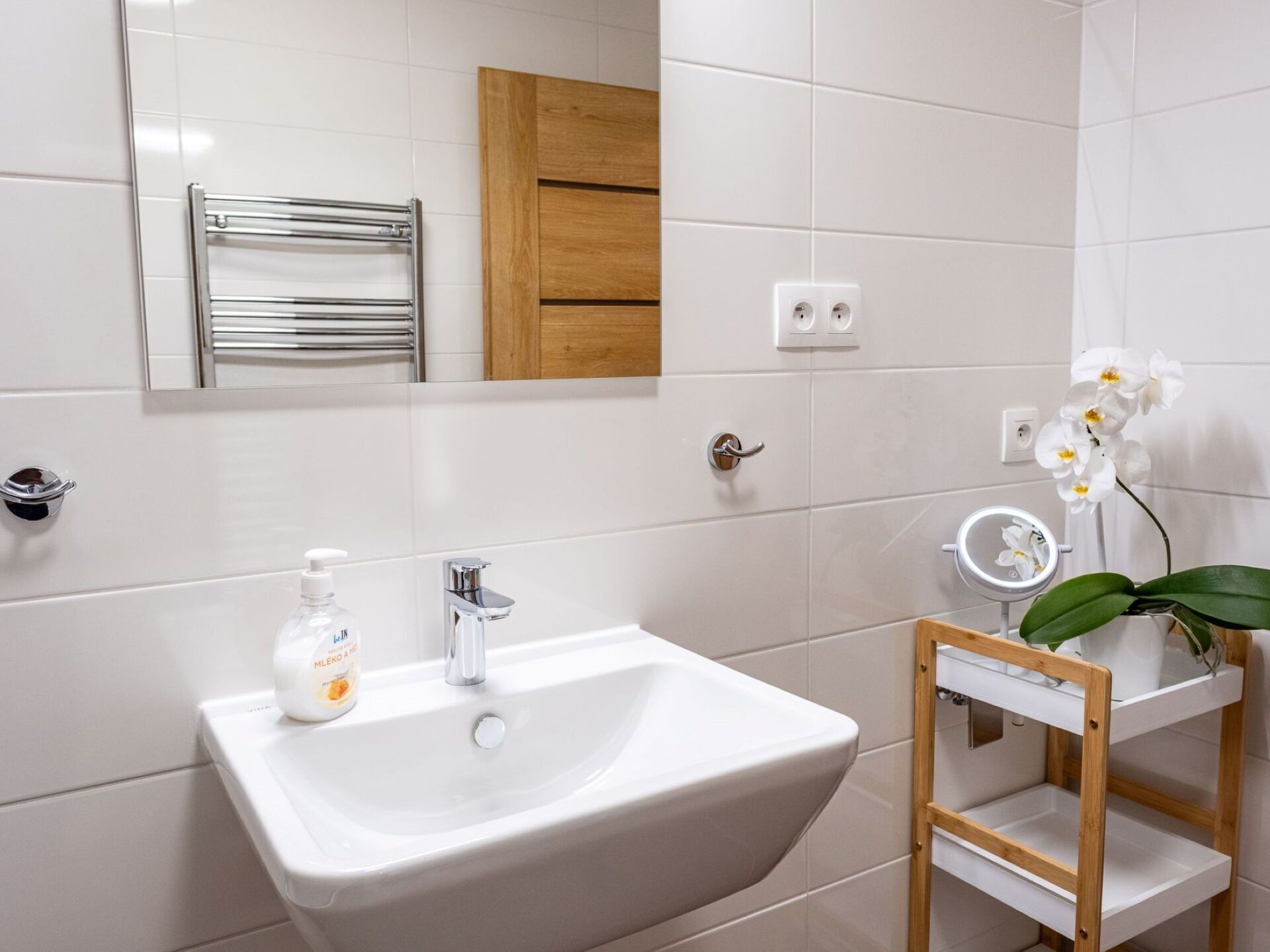 A bathroom with a white sink, mirror, and wooden cabinet.