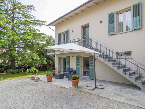 Une maison à deux étages dotée d’un patio couvert, d’un espace salon extérieur et d’un escalier.
