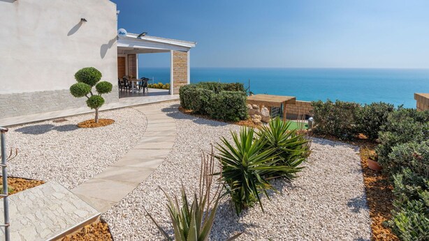 Una casa moderna con un patio que da al mar, con un pequeño jardín y una zona de estar.