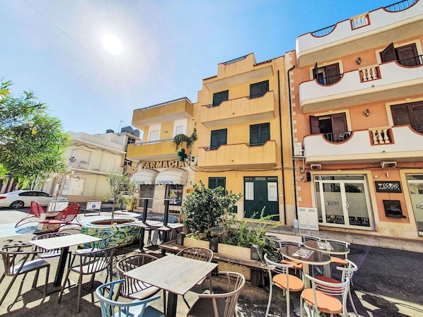 Ein Café mit Tischen und Stühlen im Freien, eine Apotheke und im Hintergrund ein Restaurant namens "Acqua Santa".