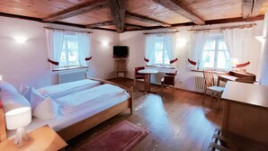 A cozy room with a wooden ceiling, a bed, a desk, a chair, and a TV. - Gasthaus zum Raben (Horben)