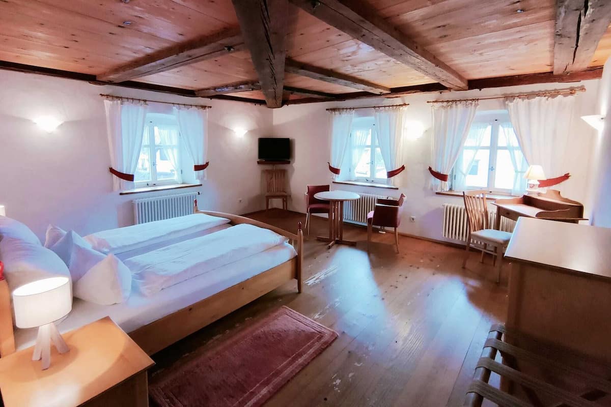 A cozy room with a wooden ceiling, a bed, a desk, a chair, and a TV.