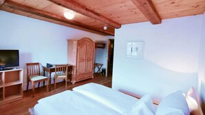 A bedroom with a wooden ceiling, a bed with white linens, a wooden wardrobe, a television, and a chair.
