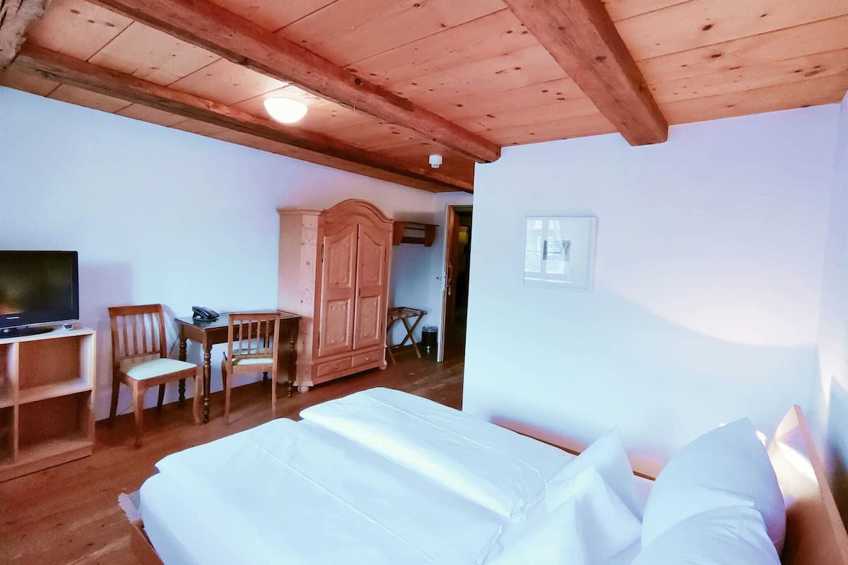 A bedroom with a wooden ceiling, a bed with white linens, a wooden wardrobe, a television, and a chair.