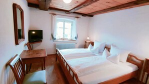 A room with a wooden bed, a television, a window with curtains, and a table with chairs.
