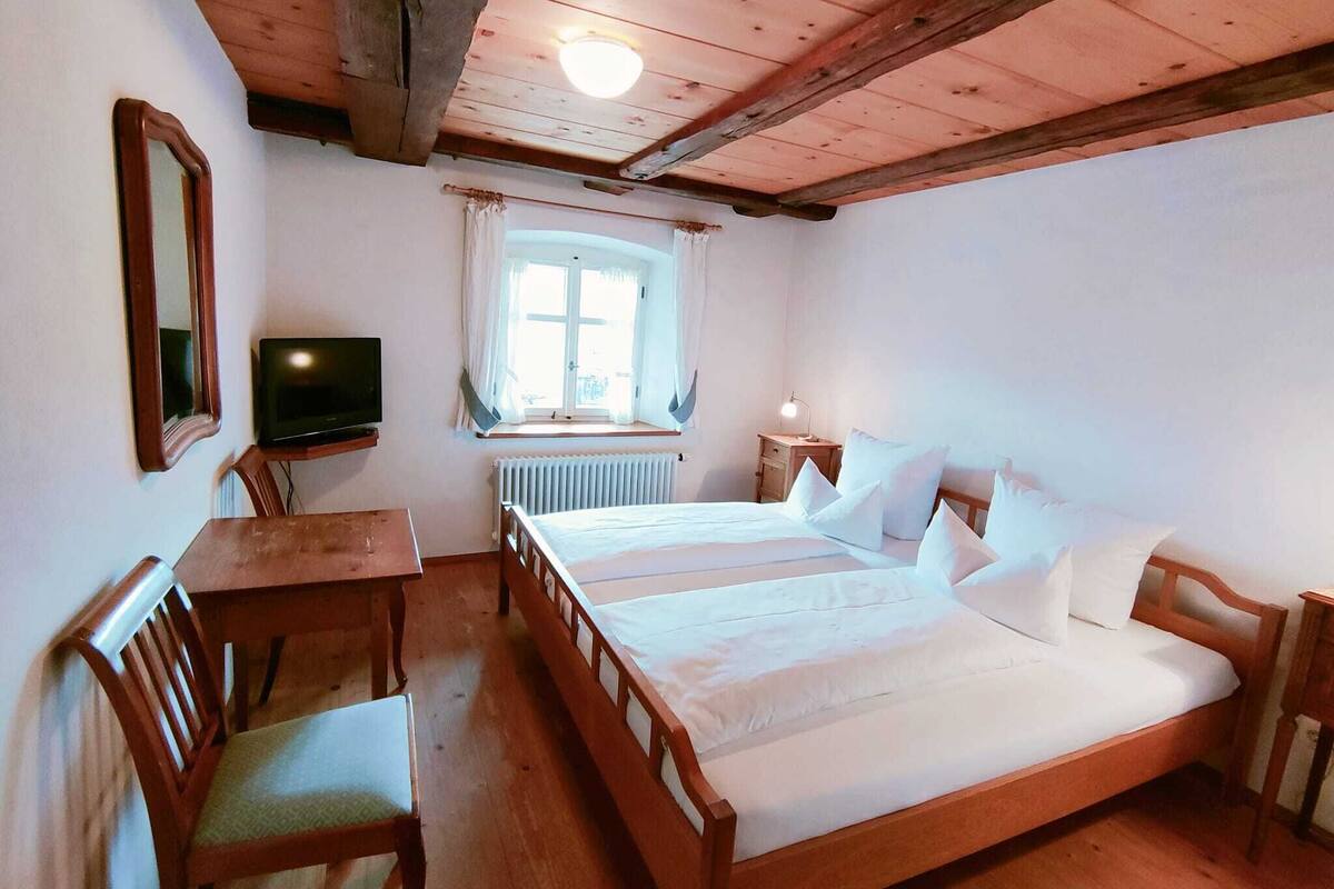 A room with a wooden bed, a television, a window with curtains, and a table with chairs.