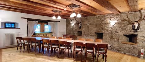 A rustic dining area with a wooden table and chairs, stone walls, and a stone fireplace.
