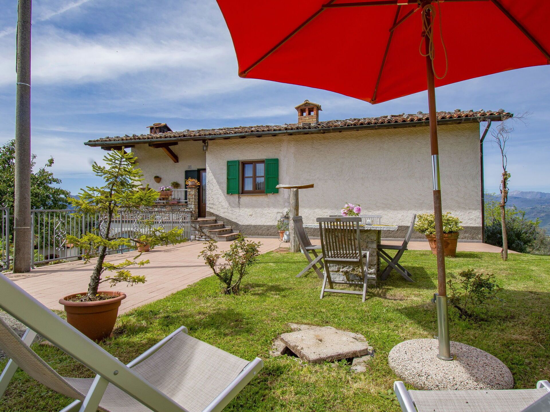 A rustic house with a stone facade, green shutters, and a patio with outdoor furniture and potted plants.