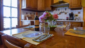 Una cocina de madera con armarios, una estufa y una mesa de comedor para dos personas, con manteles individuales y cubiertos.