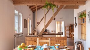 Ein Essbereich mit einem Holztisch, der für ein Frühstück gedeckt ist, einer hängenden Pflanze und einer rustikalen Küche im Hintergrund.
