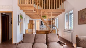 Ein gemütliches Wohnzimmer mit einer Holztreppe, einem Sofa, einem Couchtisch und einer Küche im Hintergrund.