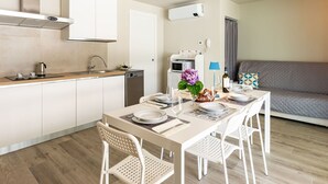 Une cuisine moderne avec des armoires blanches, un four encastré et un coin repas avec une table mise pour deux personnes.