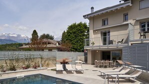 Une piscine entourée d’une clôture, avec des chaises longues et une table, et offrant une vue sur la montagne.