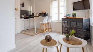 A modern kitchen with white cabinets, a dining area with white chairs, a small table with a plant, and a TV mounted on the wall. - Beautiful apartment for 2 guests with WIFI, TV and pets allowed (Louvières)