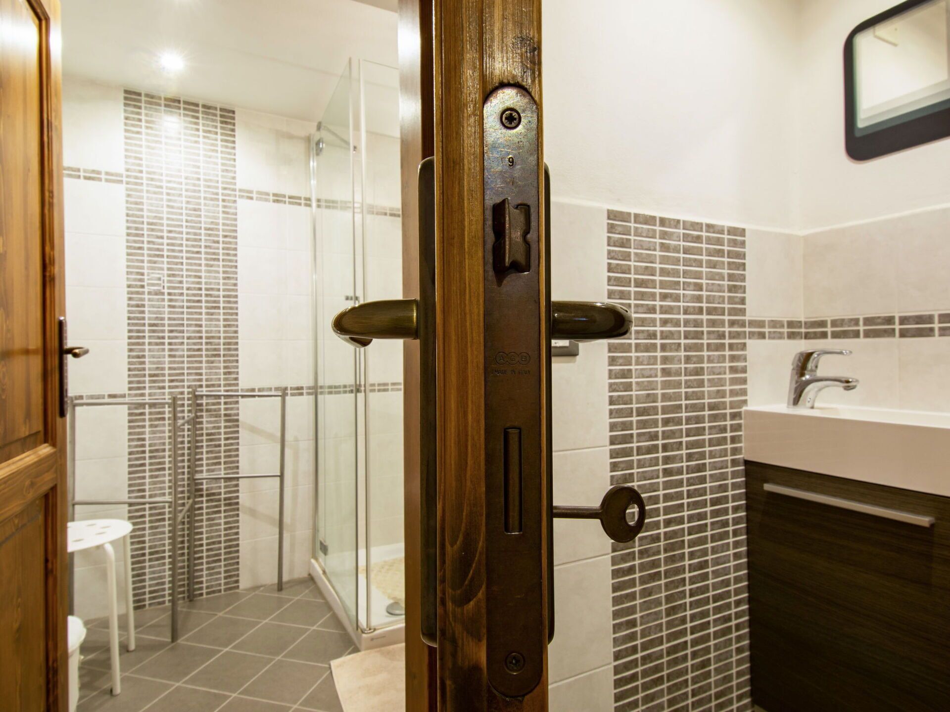 A modern bathroom with a glass shower enclosure, a wooden door, and a tiled backsplash.
