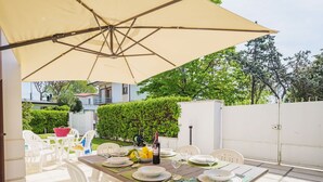 An outdoor patio with a table set for dining, surrounded by white chairs, under a large umbrella. - Beautiful private villa for 5 guests with TV and patio (Camaiore)