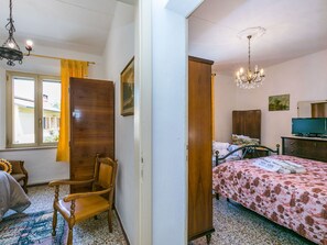 Quarto com cama, cadeira, escrivaninha, televisão e janela com cortinas.