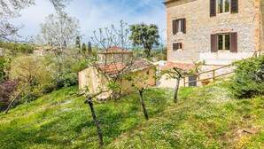 Un edificio de piedra con fachada de piedra, una escalera de madera y un jardín con árboles y flores.