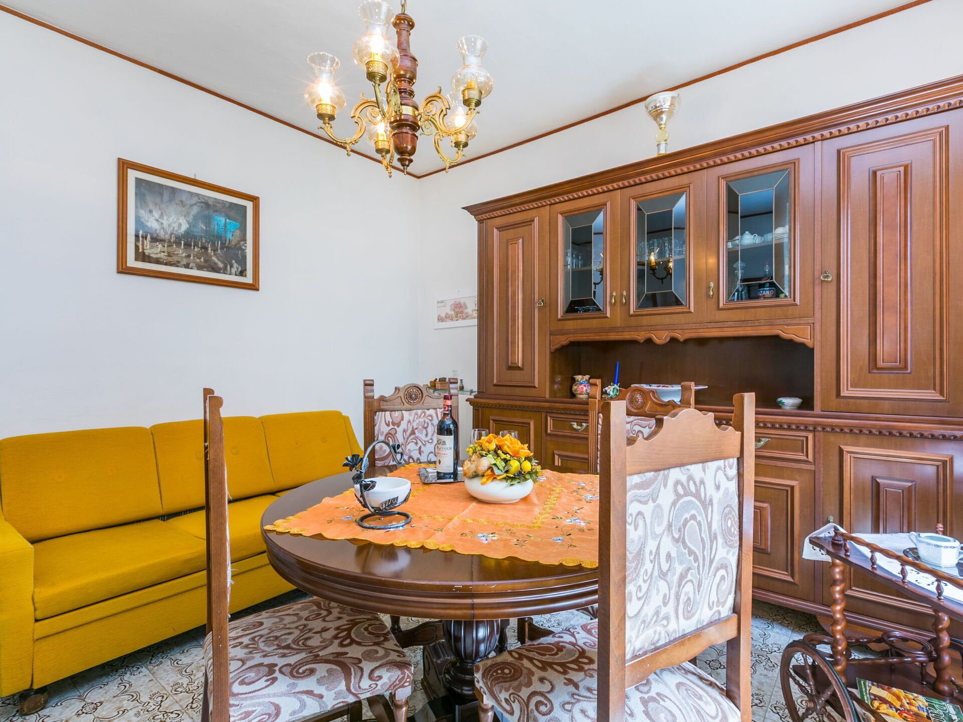 A dining area with a round table, chairs, a yellow sofa, and wooden cabinets.