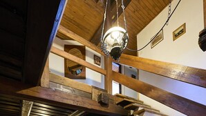 Uma sala de estar ampla, com teto alto, vigas de madeira, lareira, sofás de couro e uma mesa redonda.