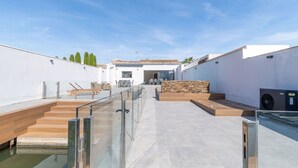 Een modern terras op het dak met een glazen balustrade, een houten dek en een stenen muur.