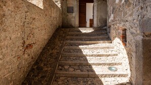 Una estrecha escalera de piedra que conduce a una puerta de madera, flanqueada por paredes de piedra tosca.