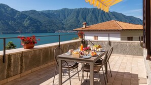 Una terraza con mesa lista para comer, con vistas a un lago y montañas.