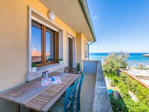 Varanda com mesa e cadeiras de madeira, com vista para um mar azul e límpido.