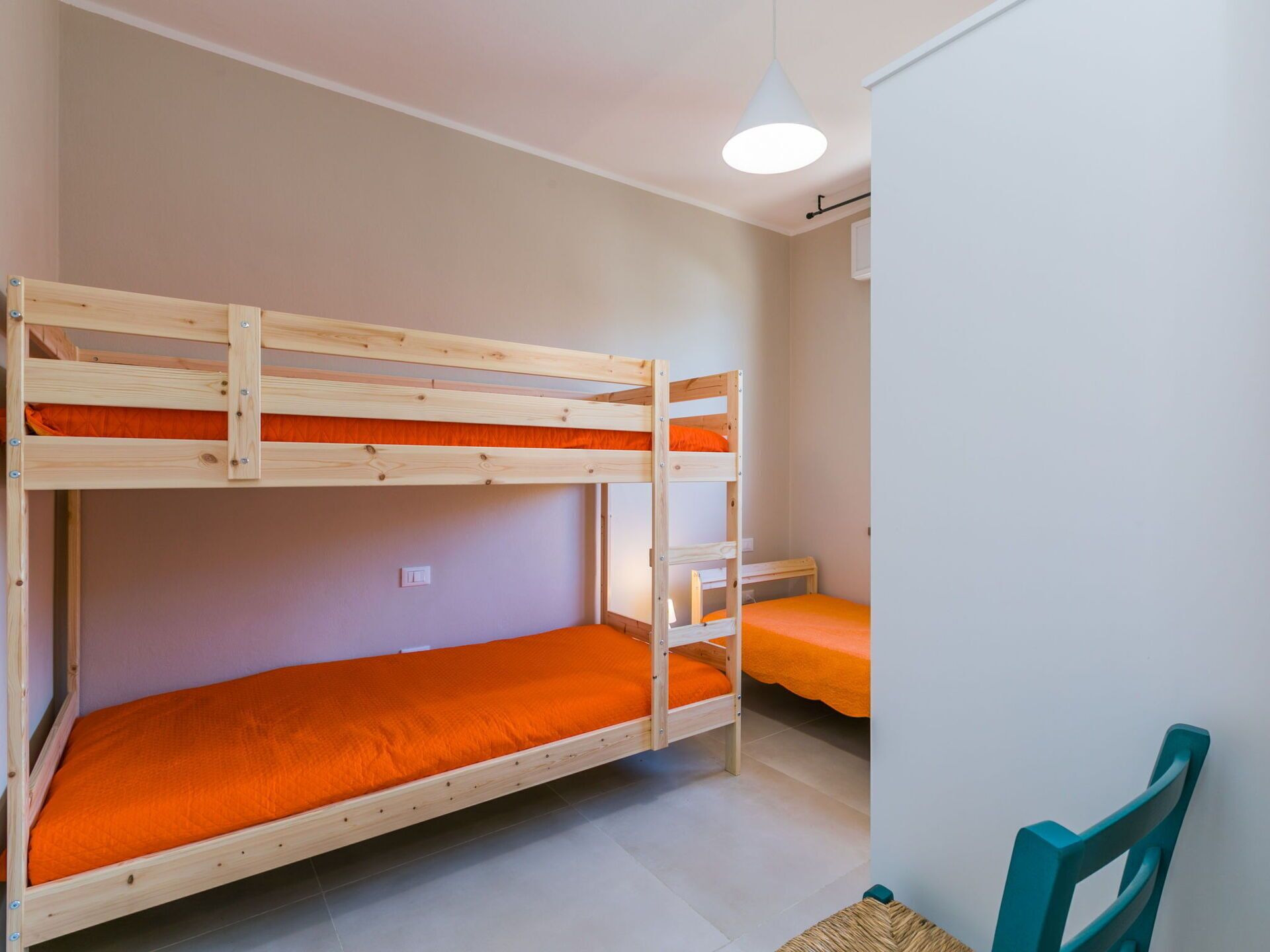 Une chambre avec un lit superposé, une couette orange, une petite table et une chaise.