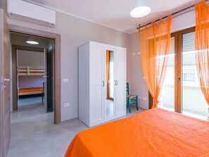 Quarto com beliche, guarda-roupa e uma janela grande com cortinas laranja.
