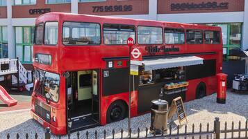 A red double-decker bus with a food stall attached, parked in front of a building with the sign "Offices" and contact number "775 96 96 96".
