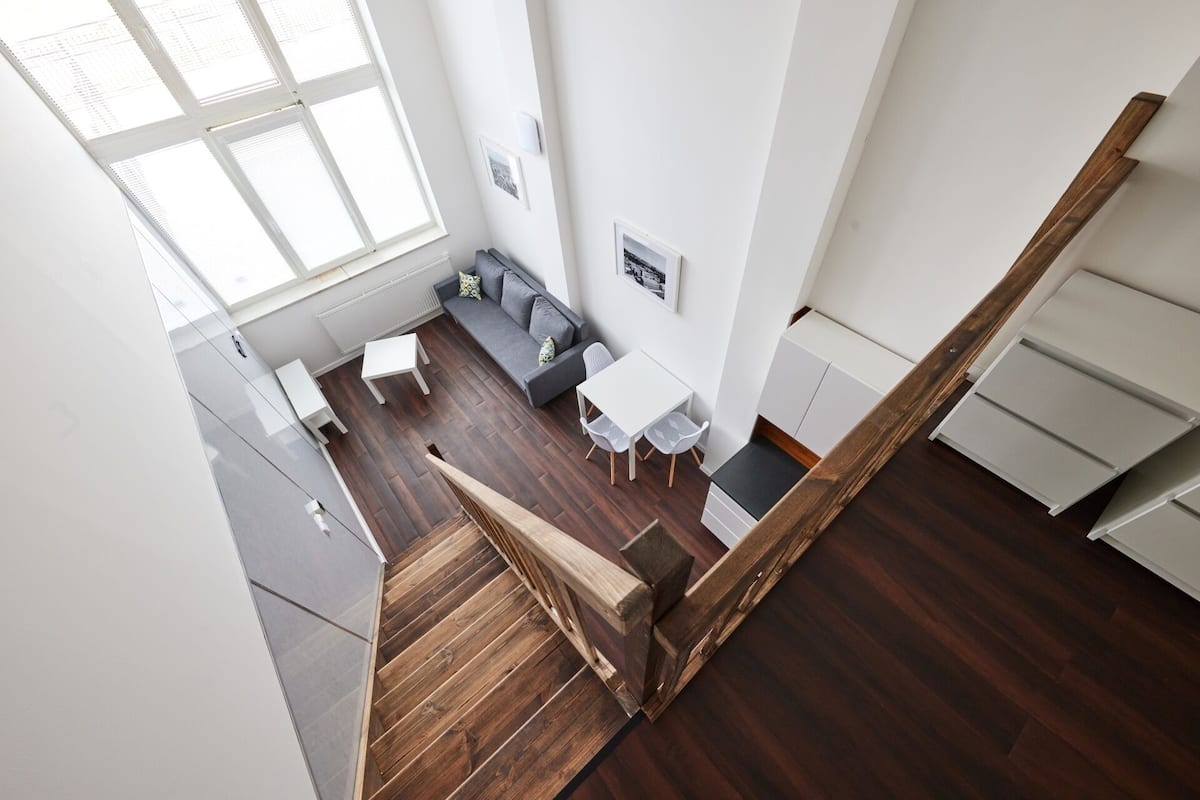 Eine moderne Wohnung mit einer Holztreppe, einem Essbereich mit weißem Tisch und Stühlen, einem grauen Sofa und einer Küchenzeile.