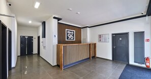 A modern reception area with a wooden reception desk, a sign indicating 'Block 96', and a fire extinguisher mounted on the wall.