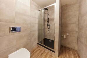 A modern bathroom with a glass-enclosed shower, a toilet, and beige tiled walls.
