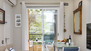 A cozy living room with a sofa, a dining table with chairs, a radiator, and a balcony with a view of trees and buildings. - Cosy apartment for 4 guests with A/C, WIFI, TV and terrace (Tossa De Mar)