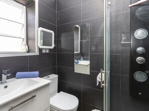 Une salle de bain moderne avec des carreaux foncés, un lavabo blanc, des toilettes, une douche en verre et un miroir au-dessus du lavabo.