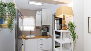 A compact kitchen with white cabinets, a stainless steel refrigerator, a microwave, and a sink. There is a window with a curtain, a shelf with a lamp, and a potted plant. - Cosy apartment for 4 guests with A/C, WIFI, TV and terrace (Tossa De Mar)