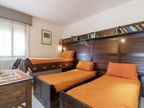 Une chambre avec trois lits, une tête de lit en bois, une petite table avec un tapis et une bibliothèque remplie de livres.