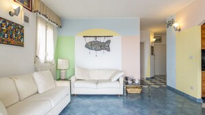 Uma sala de estar com um sofá branco, uma mesa de centro e uma obra de arte de peixe na parede.