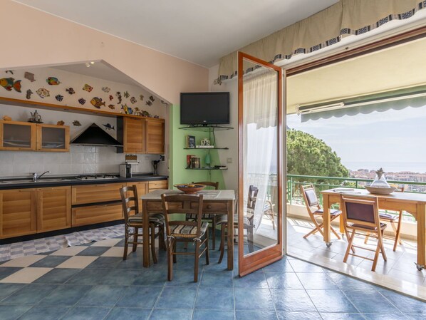 Une cuisine avec des meubles en bois, un coin repas avec des chaises et un balcon avec une table et des chaises.