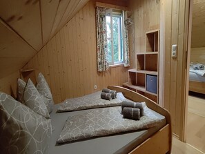 Um quarto acolhedor estilo cabana, com duas camas, uma janela com cortinas florais e prateleiras embutidas.