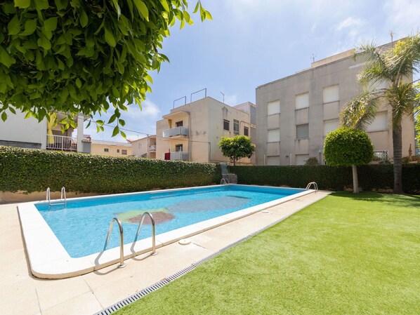 A swimming pool with a metal ladder, surrounded by a well-maintained lawn and hedges.