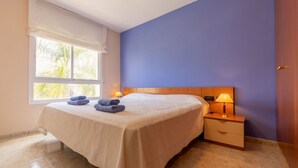 Un dormitorio con una cama, una mesita de noche, una ventana y una lámpara.