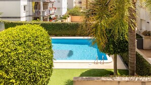 Una piscina rodeada de setos bien cuidados y palmeras, con vistas a edificios residenciales al fondo.