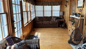 A cozy cabin interior with a wooden floor, a brown sofa, a wicker chair, and a fishing rod. - Make memories at this Big Chetac Lake Cottage (Birchwood)