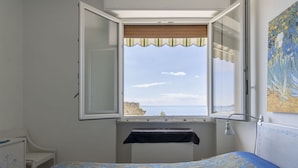 A bedroom with a bed, a window with a view of the sea, and a painting on the wall. - Nice apartment for 4 guests with A/C, WIFI and balcony (Sanremo)