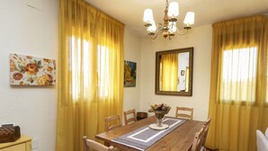 Un coin repas avec une table en bois, des chaises, des rideaux jaunes, un lustre et des œuvres d’art accrochées aux murs.