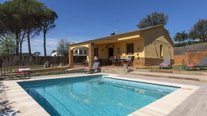 Une piscine avec des chaises longues, un espace patio et un bâtiment jaune agrémenté de pierres apparentes.