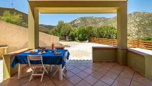 A covered outdoor dining area with a table set for two, overlooking a mountainous landscape.
