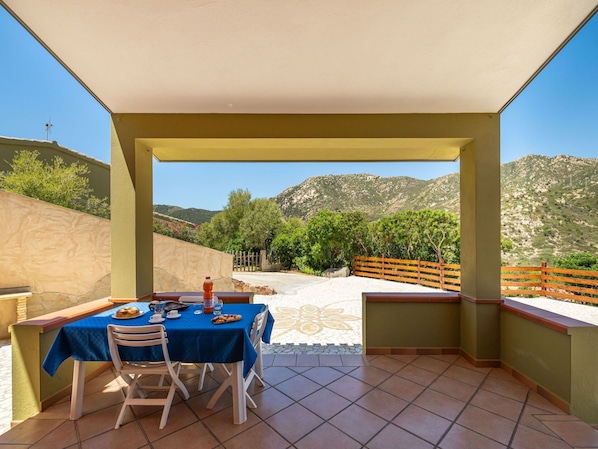 A covered outdoor dining area with a table set for two, overlooking a mountainous landscape.